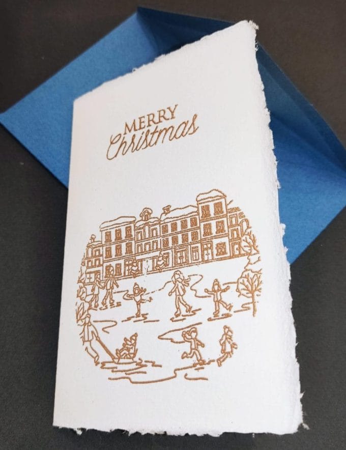 Biglietti pieghevoli in carta di Amalfi per il Natale. I decori sono realizzati con dorature a rilievo realizzate a mano da Lo Scrigno di Santa Chiara. In copertina l'illustrazione di un tipico paesaggio natalizio.