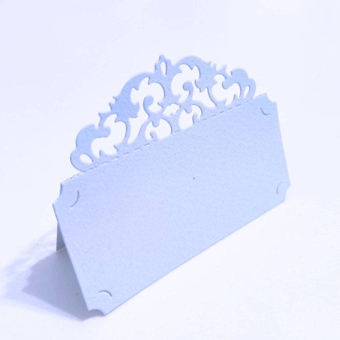 Place marker in Amalfi paper with baroque style fretwork. Pearl grey color.